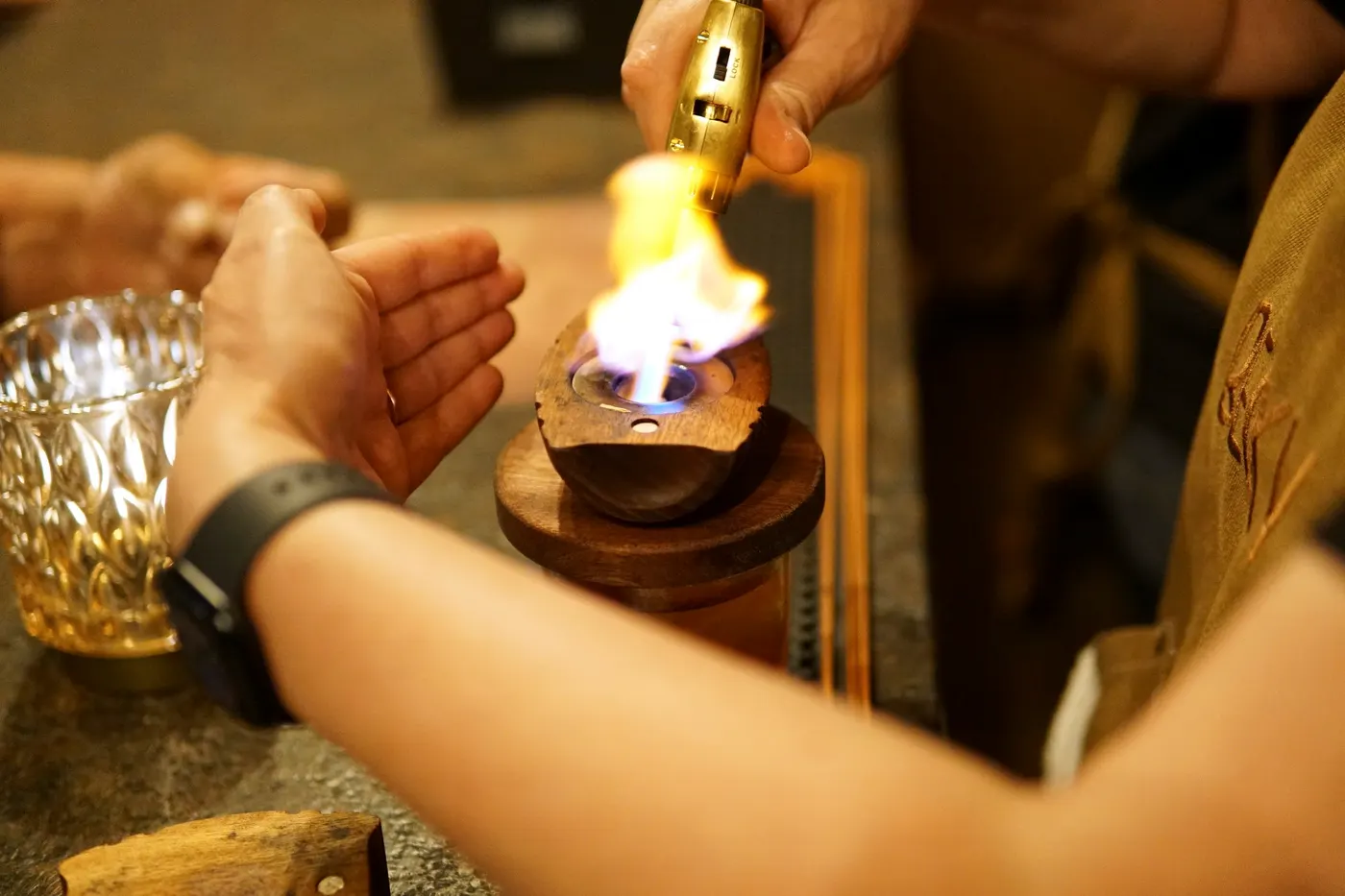 A bartender torching the smoker box over an old fashioned at the bar