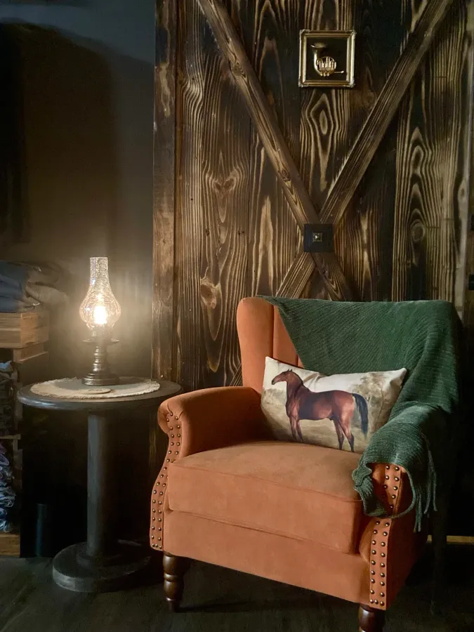 A rust velvet armchair with an oil lamp against the charred-wood wall