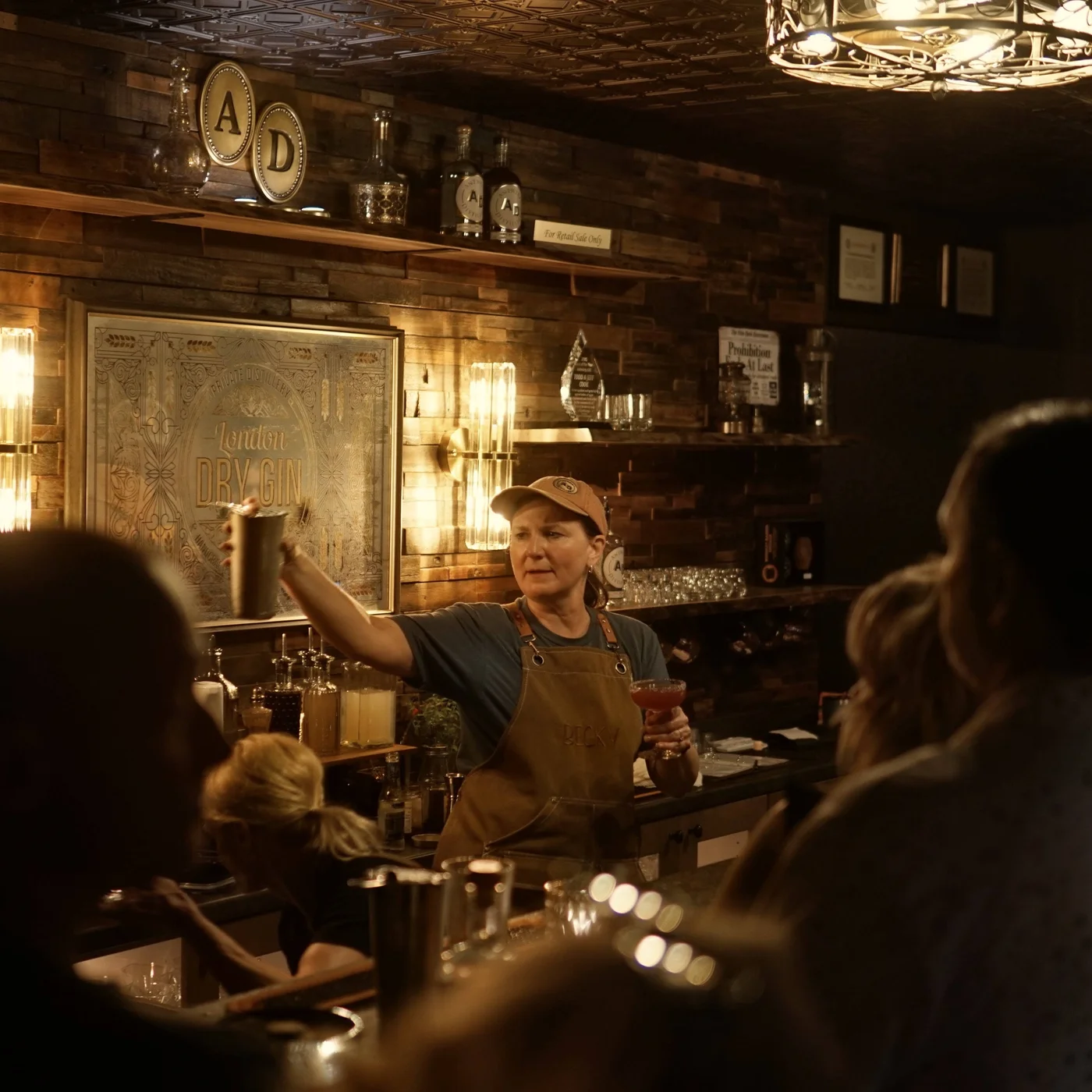 A bartender shaking a cocktail behind the bar beneath the London Dry Gin sign