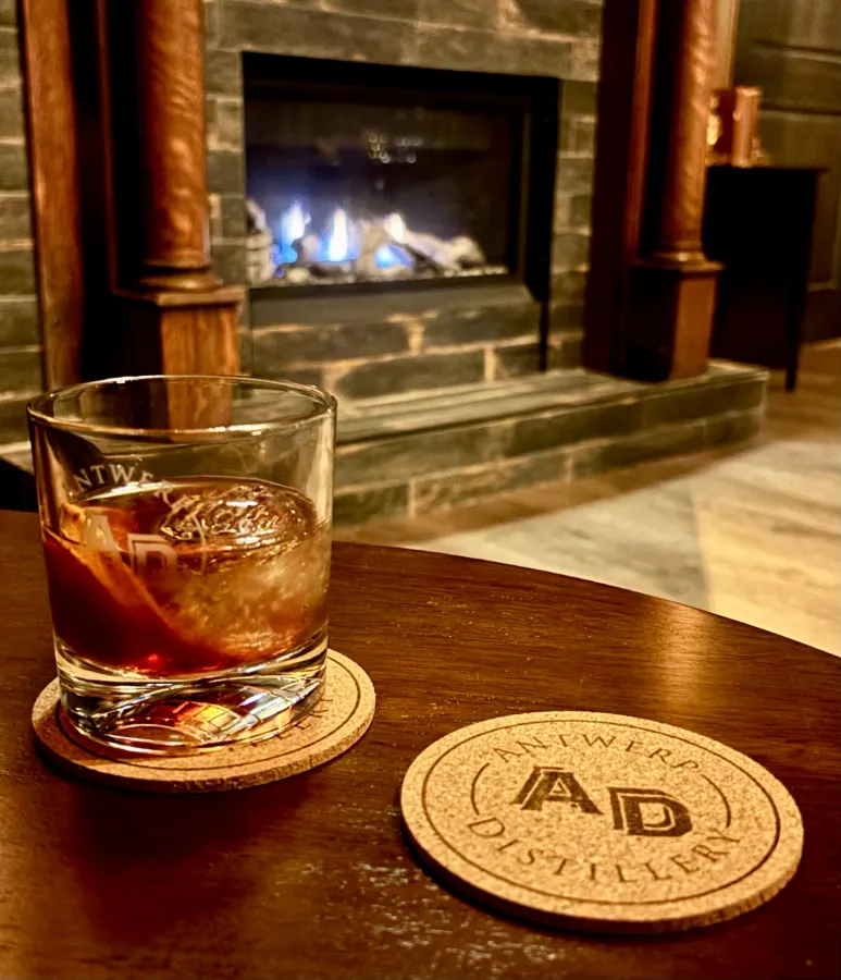 An Antwerp Distillery cocktail on the rocks beside the fireplace