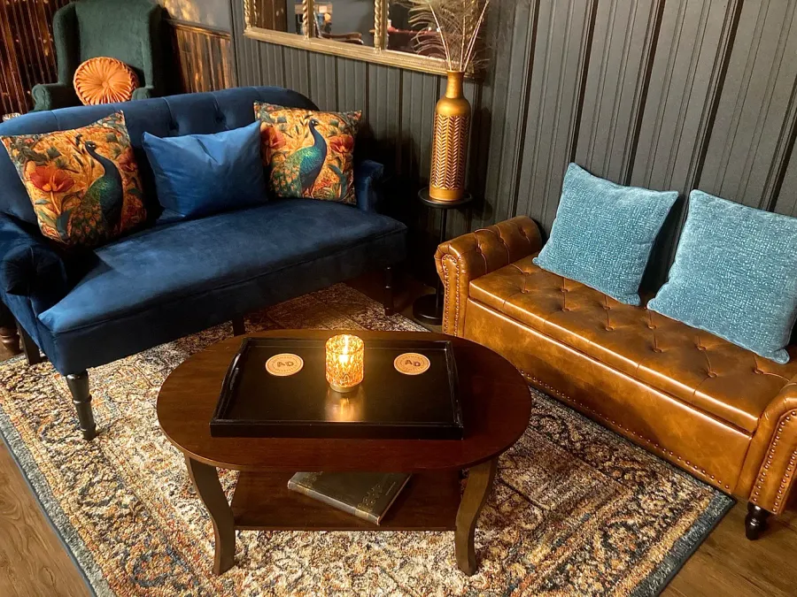 The lounge seating grouping — navy velvet sofa with peacock pillows and a tufted leather bench