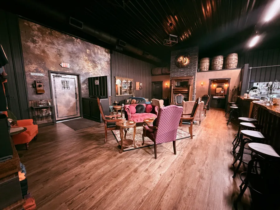The full speakeasy parlor — velvet chairs and fireplace on one side, the bar and stools on the other