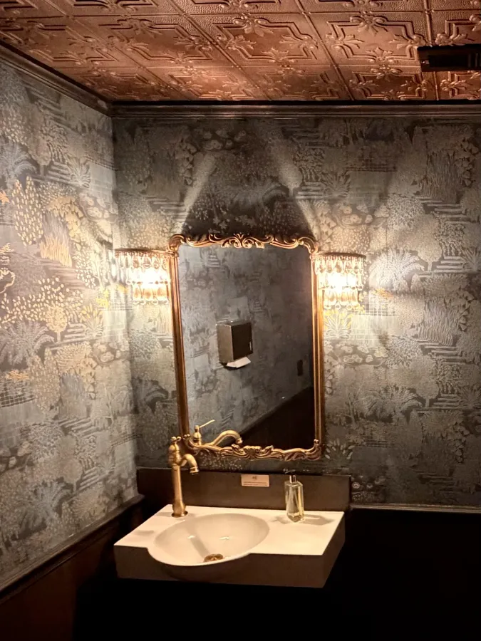 The powder room — pressed-tin ceiling, gilt mirror, and brass fixtures
