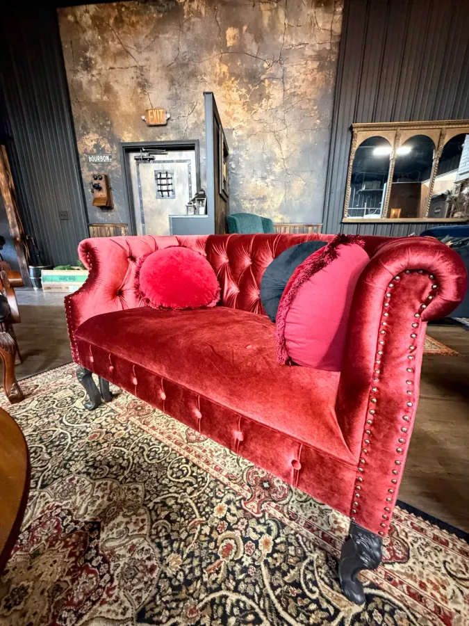 A red velvet tufted settee on a Persian rug in the speakeasy lounge