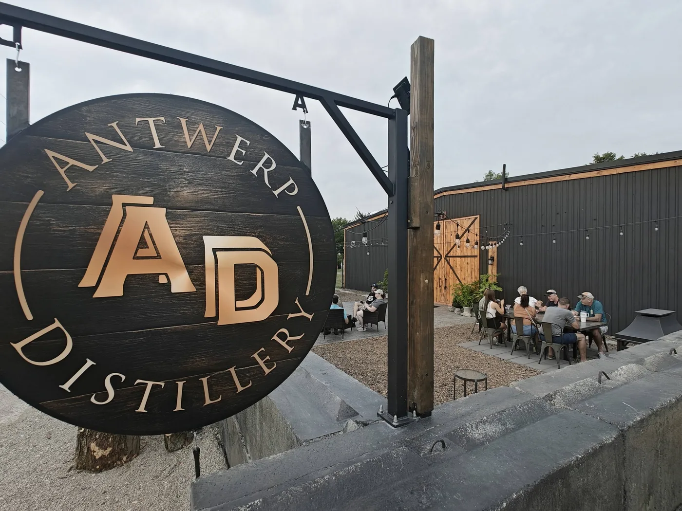 The hanging Antwerp Distillery sign with the outdoor patio and string lights beyond