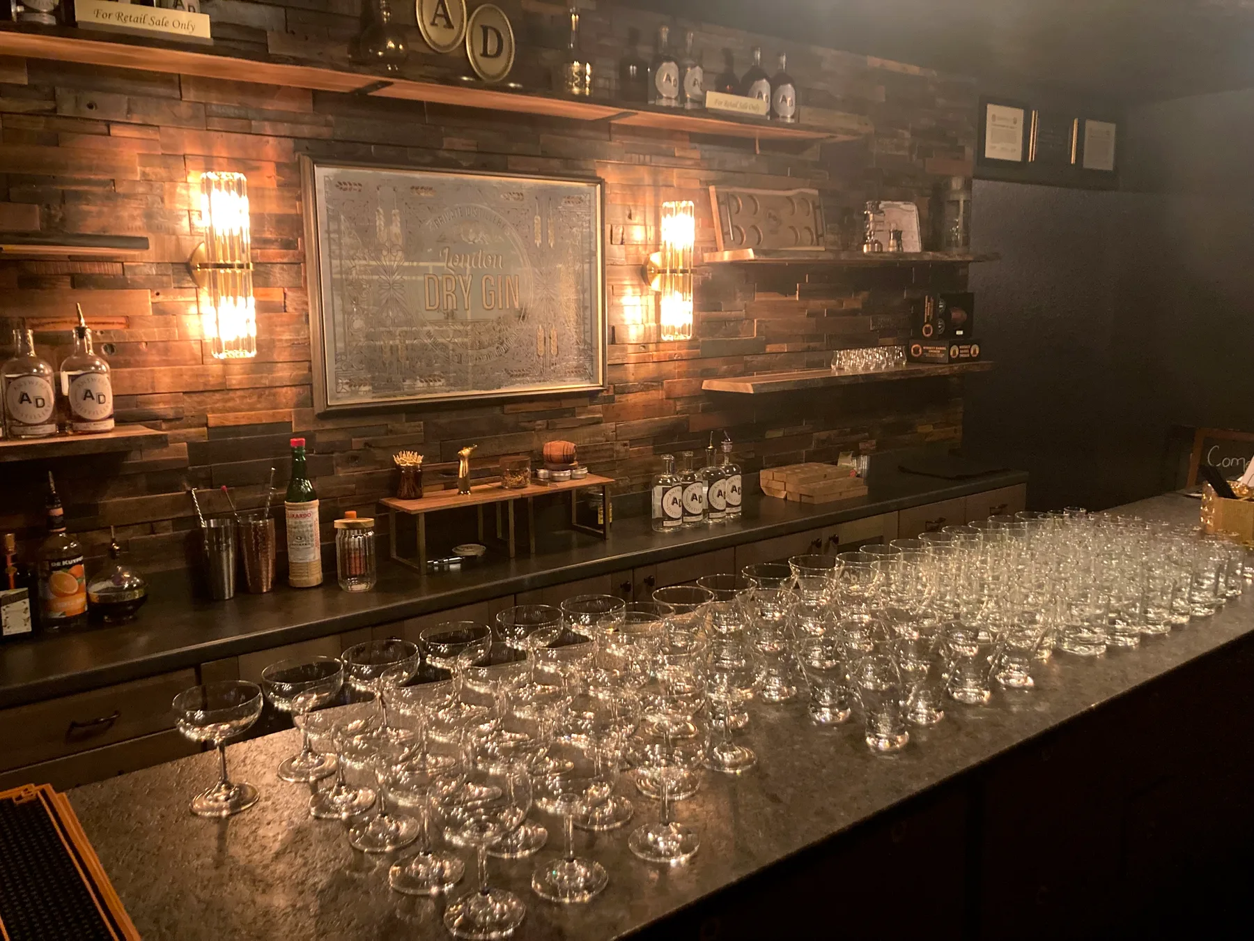 The tasting room bar set with rows of glasses under the gin mirror and prism sconces